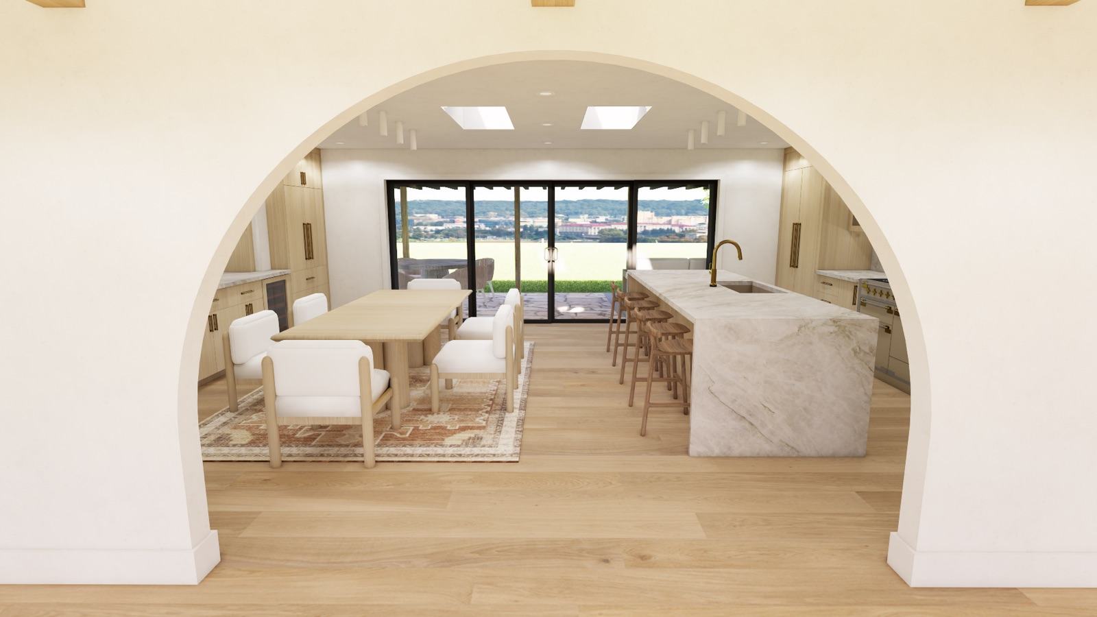 Open-plan kitchen and dining room viewed through a rounded plaster archway, with a white marble waterfall island, brass gooseneck faucet, wood-seat barstools, light oak dining table and flooring, and floor-to-ceiling sliding glass doors opening to a patio with an expansive valley view — Damn Good Interiors interior design, Denver, CO