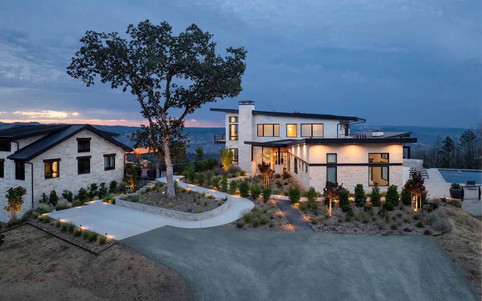 Twilight exterior of a modern stone estate with landscape lighting, hillside views, and pool — Damn Good Interiors interior design, Napa Valley, CA