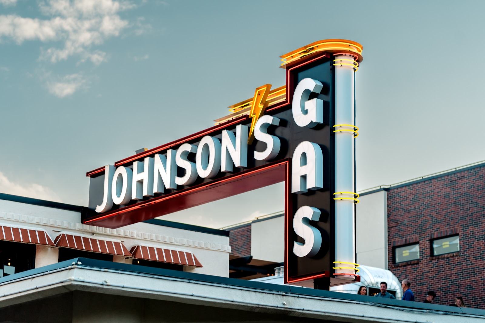 Illuminated retro neon marquee sign reading 'Johnson's Gas' with a lightning-bolt motif on the restaurant roofline at dusk — Damn Good Interiors interior design, Longmont, CO