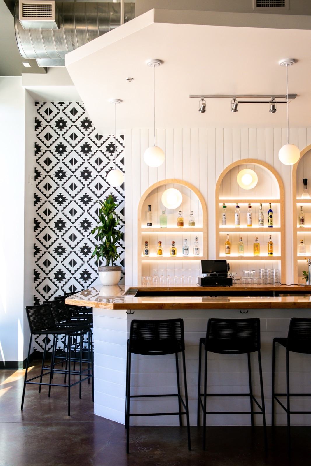 Bar with black-and-white geometric tile wall, arched backlit liquor display niches, and globe pendant lighting — Damn Good Interiors interior design, Broomfield, CO
