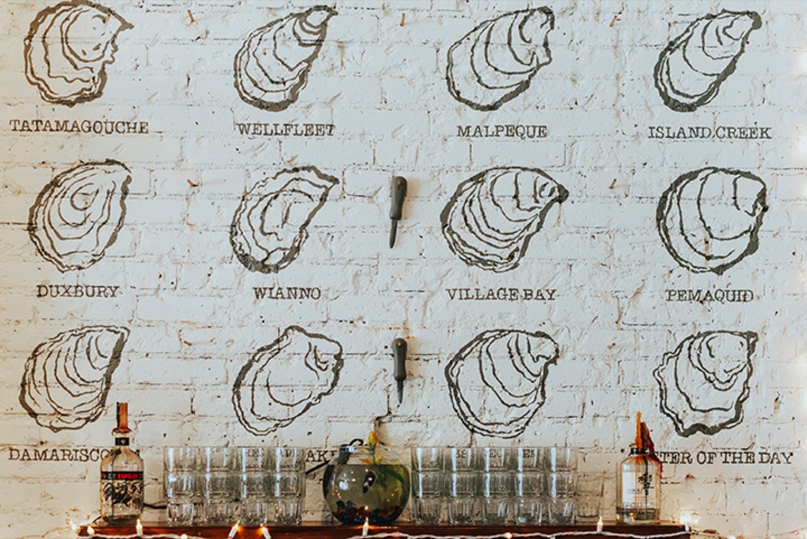Whitewashed brick wall with hand-illustrated oyster varietals and lettering above the raw bar — Damn Good Interiors interior design, Fort Collins, CO
